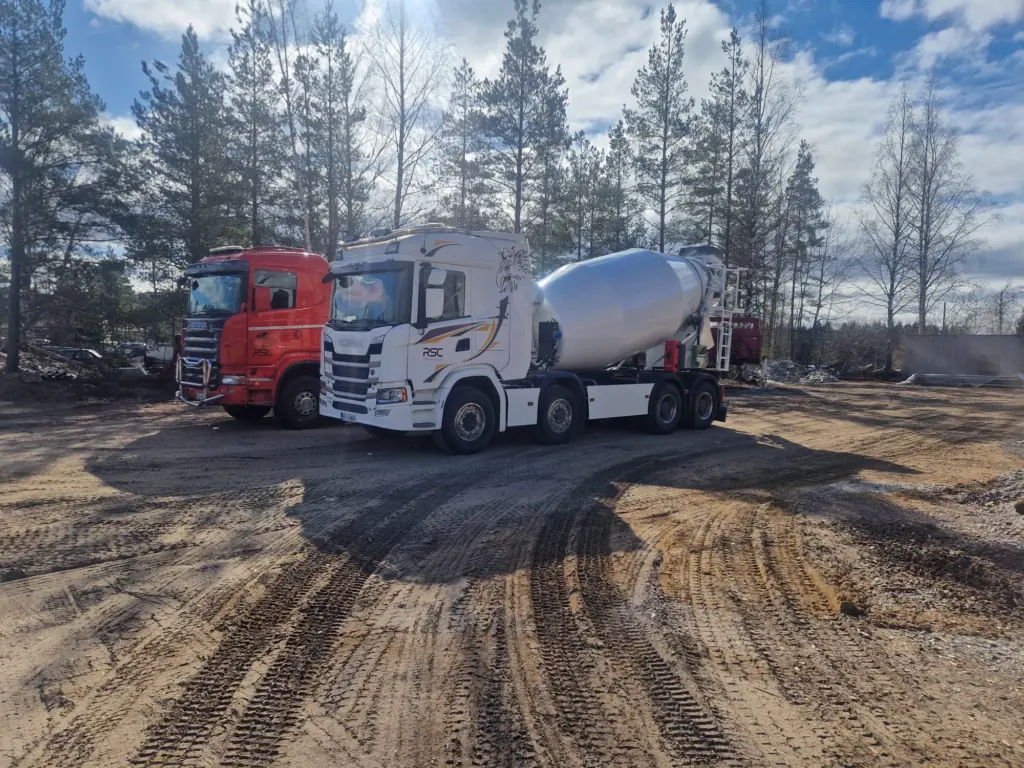 Valkoinen betoniauto ja punainen kuorma-auto työmaa-alueella